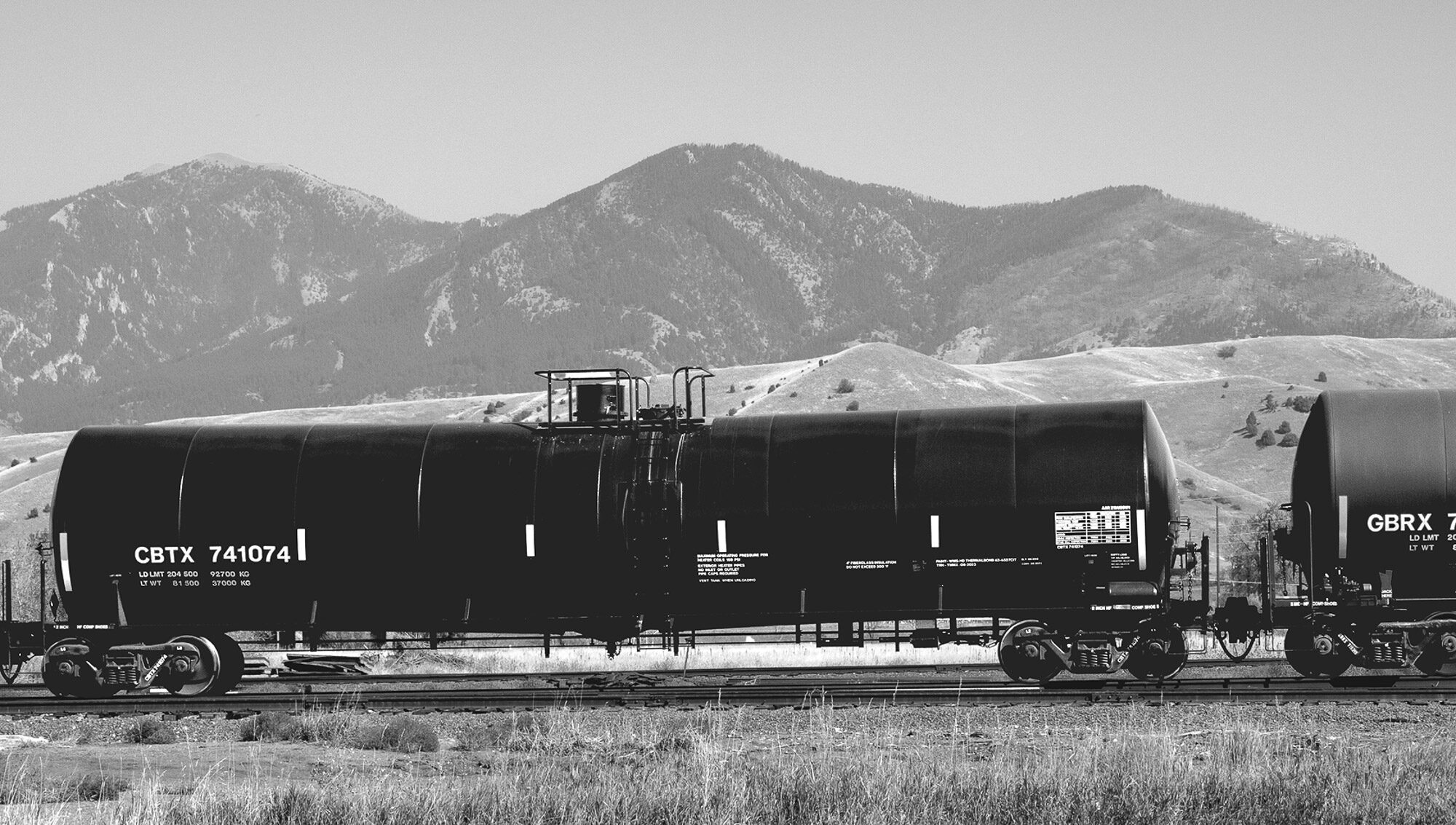 black and white image of an oil train car with the mountains in the background