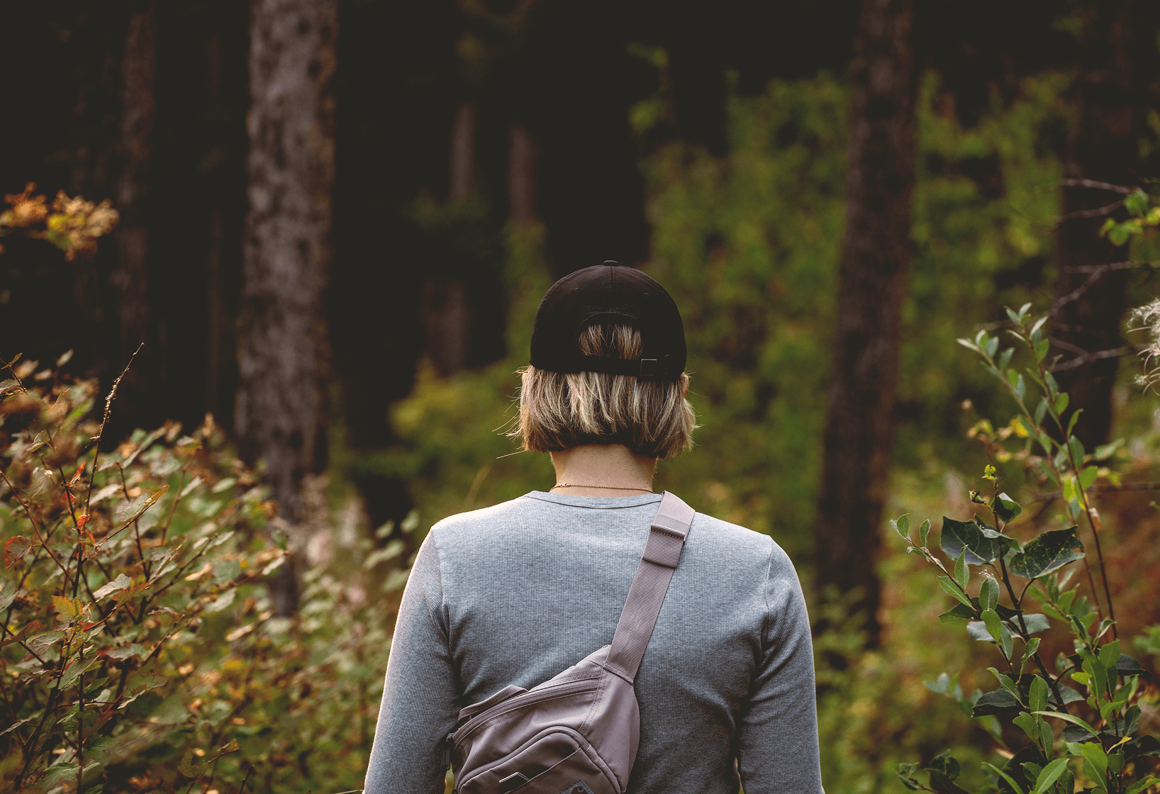 image from behind of a woman wearing a baseball hat walking in the woods