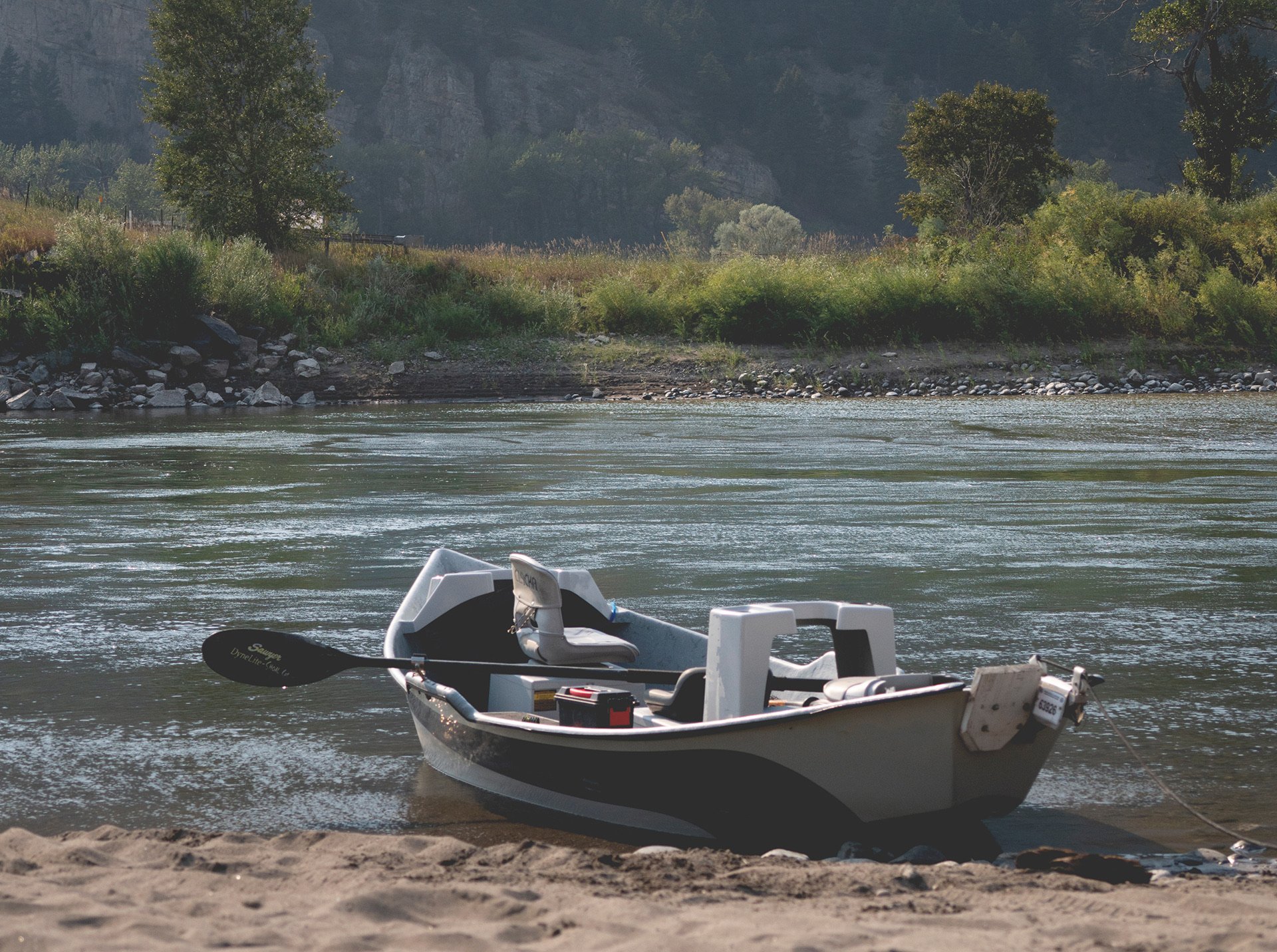 small boat along the bank of a river with trees on the other side of the river