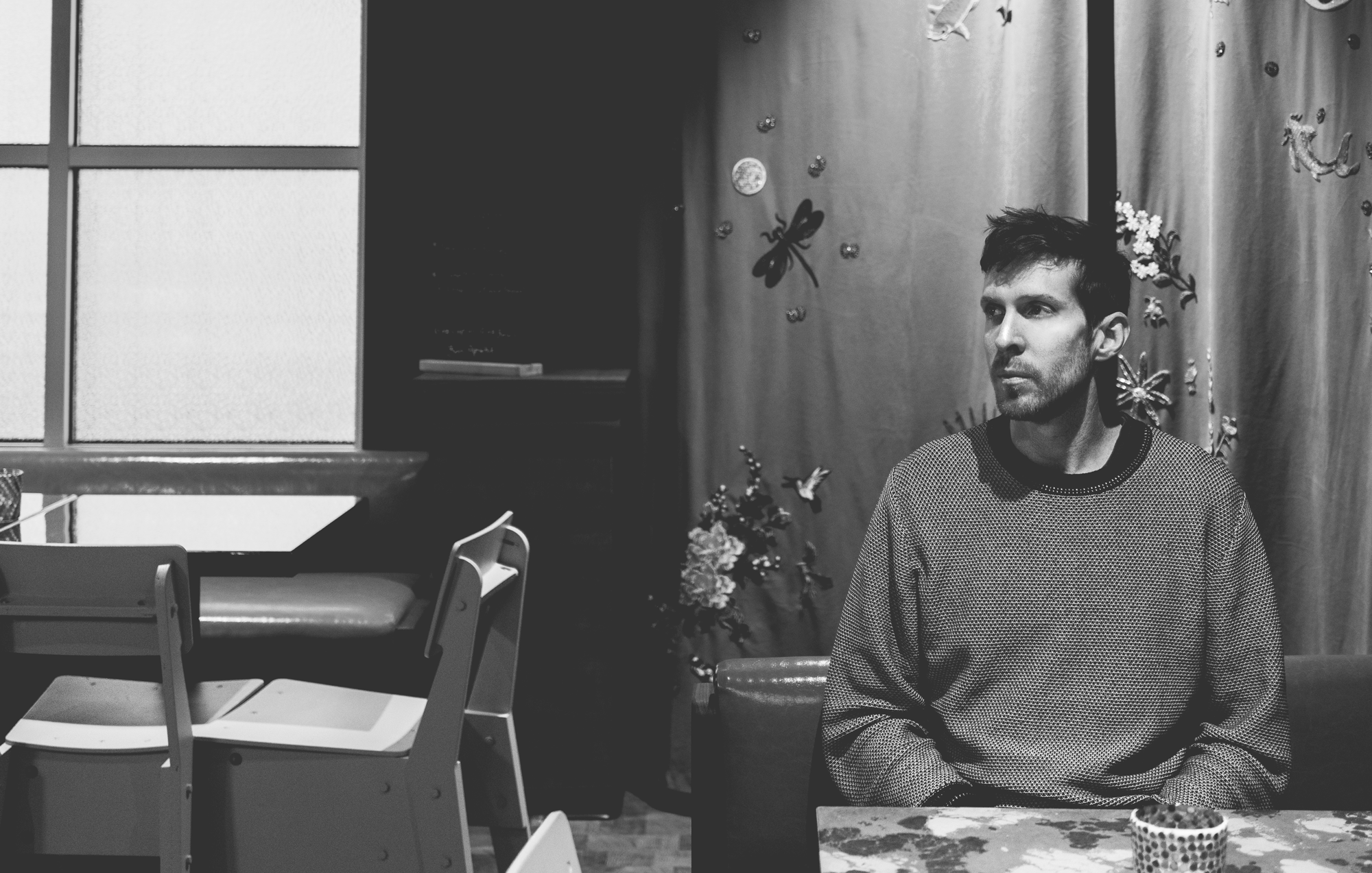 black and white image of a man sitting in front of curtains with flowers on them