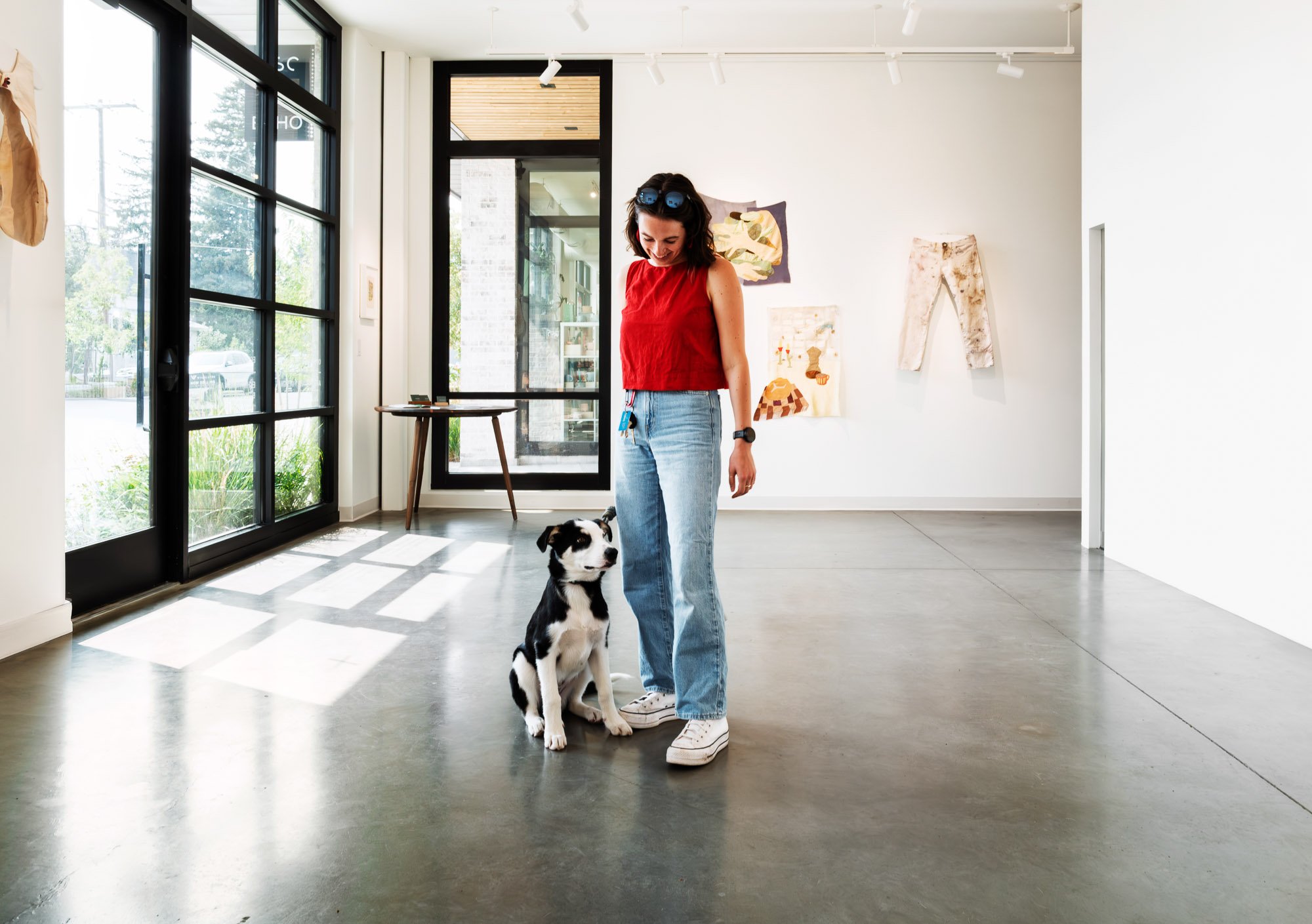 woman with a black and white dog inside Echo Arts gallery with artwork on a wall in the background