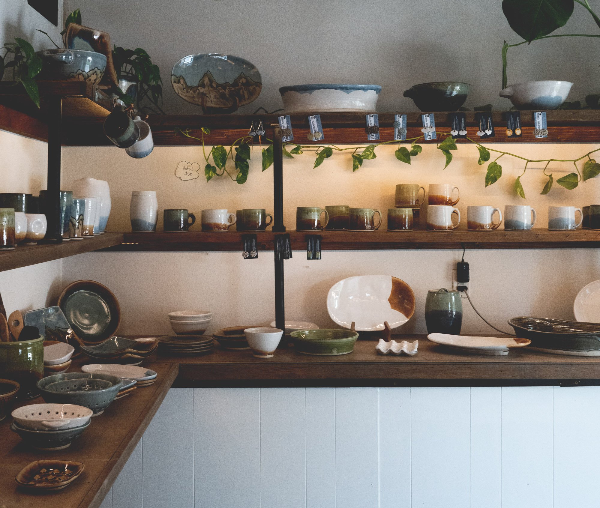 three shelves displaying handmade pottery items such as mugs, bowls, and serving plates